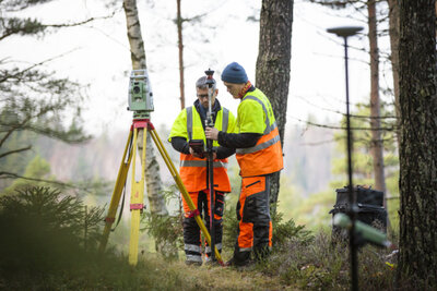 Två personer iförda reflexväst som arbetar med ett mätinstrument i skogen