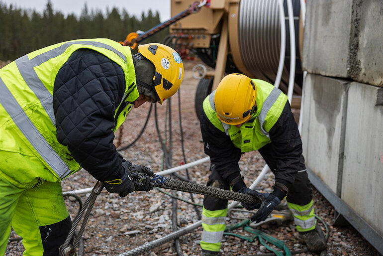 Två personer i gula varselvästar som lutar sig fram och gör en sprängskarvning.