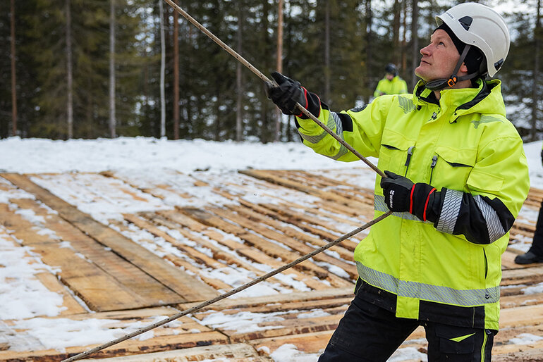 En man deltar i en stolpresning vid Aurora Line i Norrbotten. Han håller i en lina. 