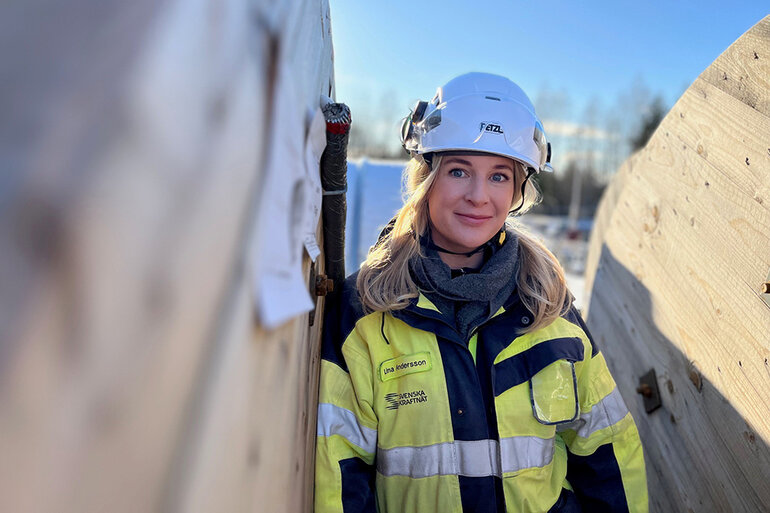 Lina står mellan två betongfundament, solen skiner, himlen är blå och hon ler.